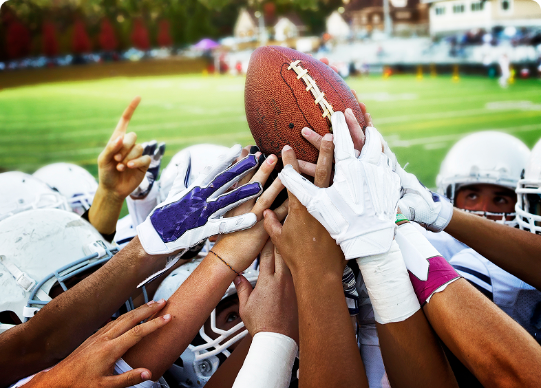 Football team huddles, holding a football.
