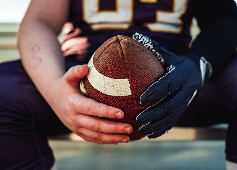Hands holding an American football ball.