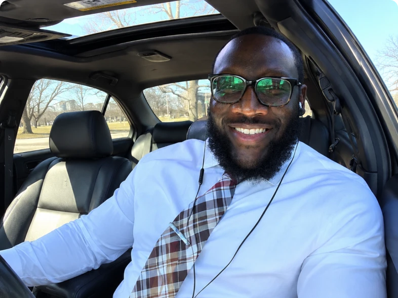 Smiling man in car wearing glasses, tie.